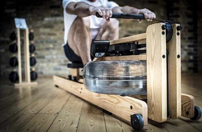 A man rowing on the WaterRower machine in a light wood stain